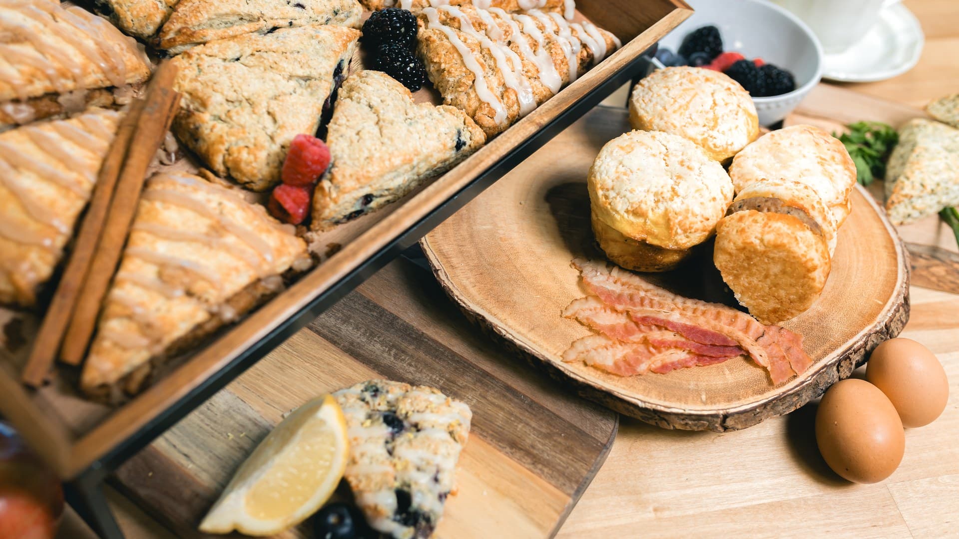Handmade scones on wooden boards with fresh berries, bacon, eggs and a white cup and saucer