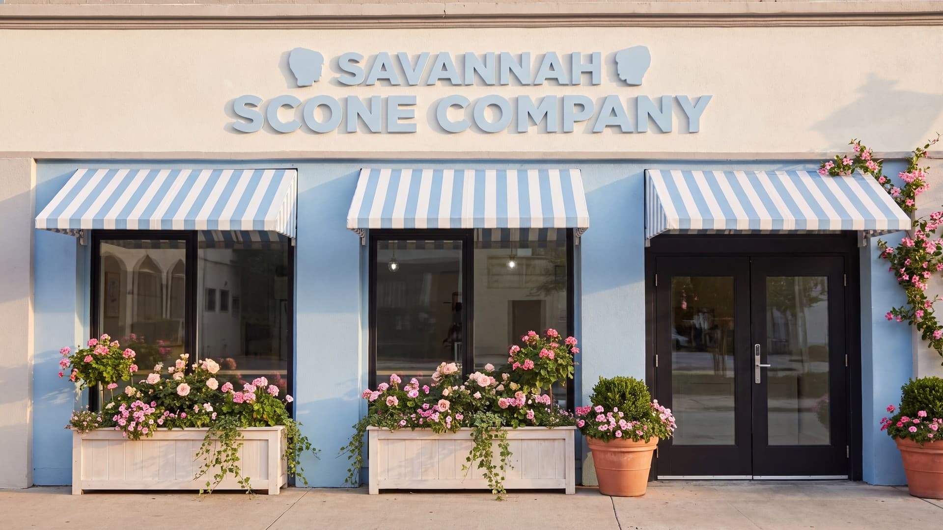 The powder blue storefront of Savannah Scone Company with striped awnings and window boxes of pink flowers.
