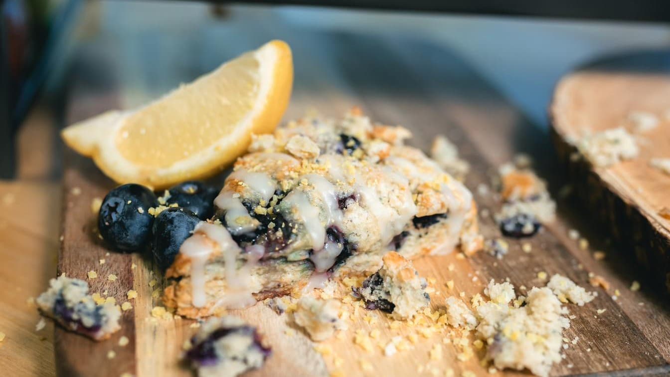 A blueberry scone broken open on a wooden board, showing its crumbly interior